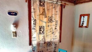 Ein Essbereich mit Holztisch und türkisfarbenen Stühlen, einem Vorhang mit Paris-Motiven, einer Wandleuchte und einem gerahmten Bild.