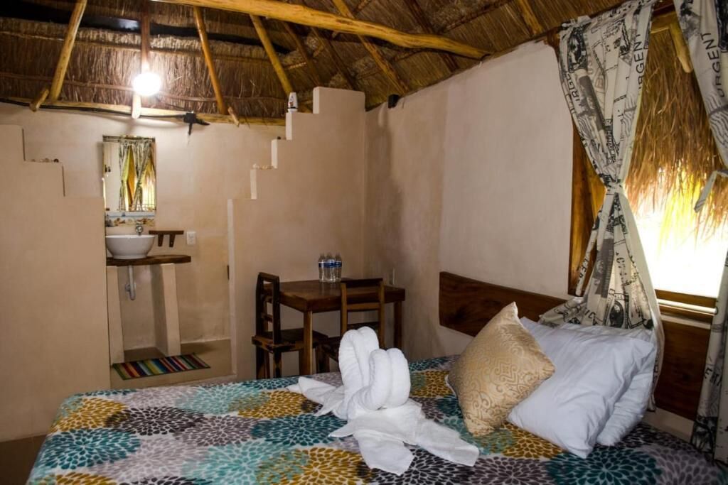 Una habitación con una cama, una mesita, una silla, un lavabo y un espejo.