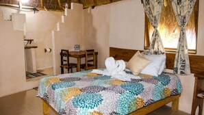 Ein Schlafzimmer mit Bett, Holz-Kopfteil, Fenster mit Vorhängen, einem kleinen Tisch mit Stuhl und einer Treppe, die zu einer oberen Ebene führt.