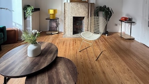 A modern living room with a fireplace, a round wooden table, a wire chair, and a large mirror on the wall. - CHAMBRE LE PHARE (Boulogne-sur-Mer)