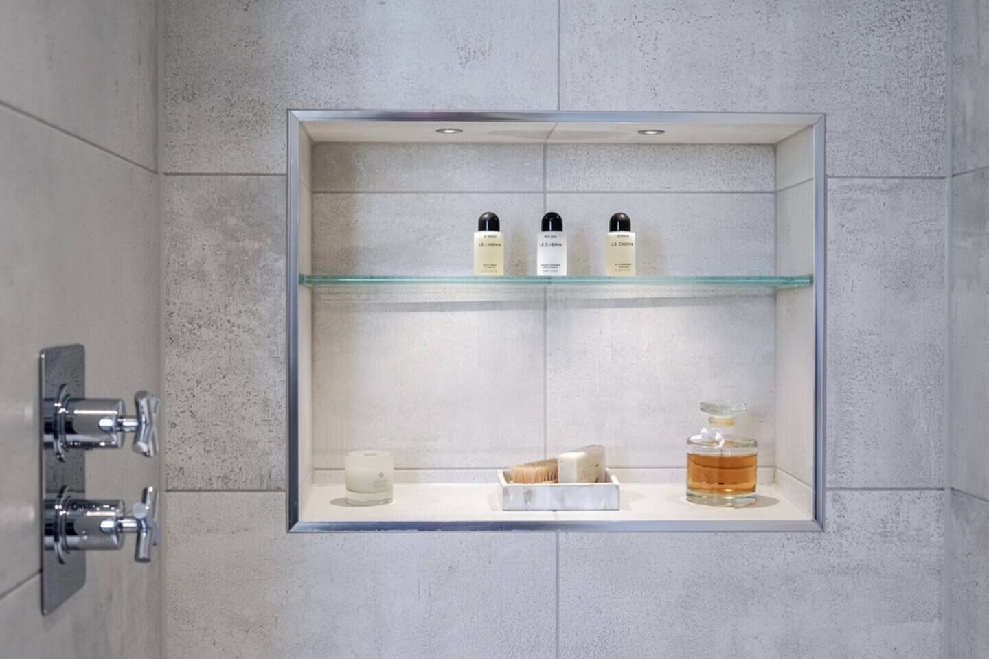 Ein Badezimmer mit einer Glastrennwand und einer Ablage mit Pflegeprodukten, einer Kerze und einer Flasche.