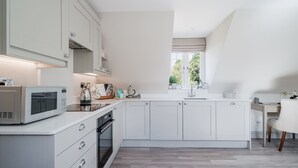 Una cocina moderna con armarios blancos, horno empotrado y microondas. Se aprecia una ventana con vista a áreas verdes.