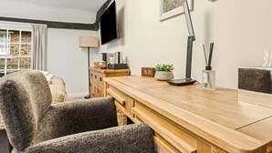 Uma sala de estar moderna com uma mesa de centro de madeira, uma poltrona cinza, uma TV fixada na parede, um abajur e uma pequena planta em vaso.