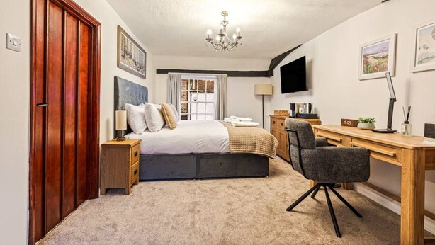 Quarto com cama, escrivaninha, cadeira e televisão na parede.