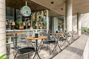 An outdoor cafe area with metal chairs and tables, a coffee machine, and potted plants. - Foodhall | Gym | 450m from the Mall #CA98 (Florianópolis)