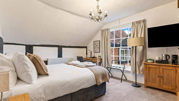 A bedroom with a large bed, a desk, a chair, a TV, and a window with curtains. - The George Inn Rooms - Room 5 (Great Missenden)