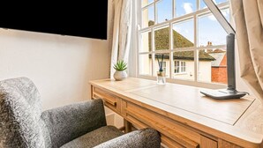 A room with a wooden desk, a chair, a TV mounted on the wall, and a window with curtains.
