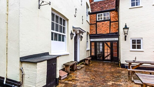 A courtyard with a brick floor, a white building with a black door, and a sign for 'The George Hotel'.