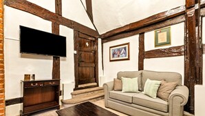 A cozy living room with exposed wooden beams, a flat-screen TV, a sofa with cushions, and a wooden coffee table. - The George Inn - Room 4 (Great Missenden)