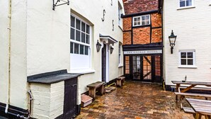 A courtyard with a brick floor, a white building with a black door, and a sign for "The George Hotel". - The George Inn - Room 4 (Great Missenden)