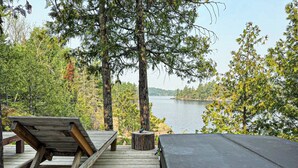 A wooden deck with a bench and a covered area, overlooking a lake surrounded by trees. - Stunning, Rustic Cottage on Lake of the Woods! (Kenora)
