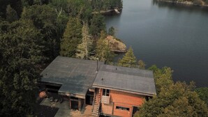 A cabin with a sloped roof, a deck, and a small porch. - Stunning, Rustic Cottage on Lake of the Woods! (Kenora)