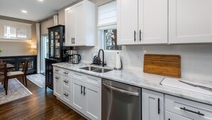 Une cuisine moderne avec des meubles blancs, des appareils en acier inoxydable et une planche à découper en bois.