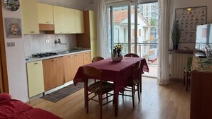 A compact kitchen with yellow cabinets, a dining table with a red tablecloth, and a view of a balcony with a building in the background. - Guest Access🌊 Jesolo – Condominio Venezia Apartment✨ Perfect for Families and Groups, Just Steps from the Sea!Welcome to your ideal retreat in Jesolo, where golden sand and crystal-clear sea await you less than 1 minute from your door! 🌅 If you (Lido di Jesolo)