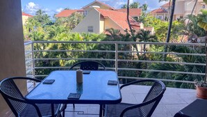Ein Balkon mit Tisch und Stühlen, mit Blick auf eine Wohngegend mit Palmen und Häusern.