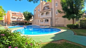 A pool surrounded by a well-maintained lawn and a building with balconies. - 2BR Apartment Center of Torrevieja (Torrevieja)