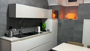 Een moderne keuken met witte kasten, een inbouwoven en een kleine eethoek met een tafel en stoelen.