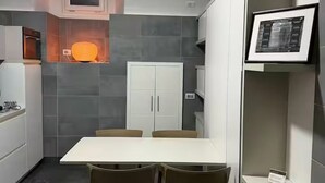 Een moderne keuken met grijze tegels, een wit kastje en een tafel met stoelen.