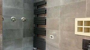 Een moderne badkamer met grijze tegels, een zwarte handdoekhouder en een klein kastje.