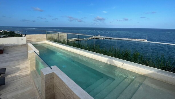 A modern infinity pool with a clear view of the ocean and a jetty extending into the water. - Studio 104 in Distrito Puerto (Puerto Morelos)