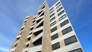 A modern high-rise building with multiple floors, large windows, and a flat roof. - Studio 104 in Distrito Puerto (Puerto Morelos)