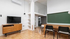 A modern classroom with a wooden cabinet, a flat-screen TV, a chalkboard, and black chairs. - RentPlanet - Apartament Krucza (Warsaw)