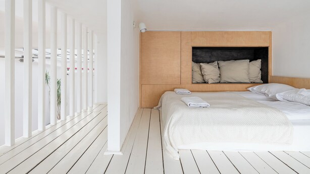 A hotel room with a wooden headboard, a large bed with white linens, and a white floor. - RentPlanet - Apartament Krucza (Warsaw)