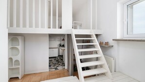 A white interior with a loft bedroom, a kitchen area, and a window. - RentPlanet - Apartament Krucza (Warsaw)