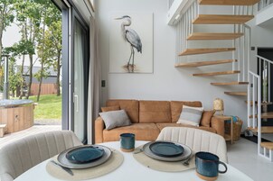 Una sala de estar moderna con un sofá marrón, una mesa de comedor con platos y una taza, y una escalera con estantes de madera.