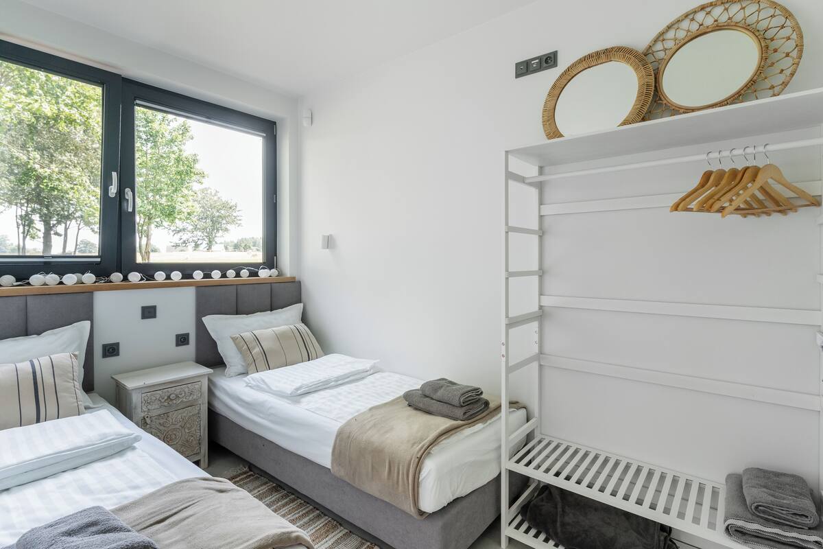 A bedroom with two beds, a wardrobe, and a window with a view of trees.
