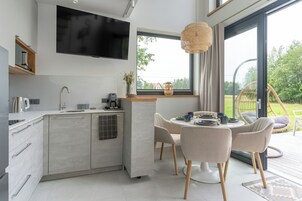 Una cocina moderna con televisor integrado, un área de comedor con sillas y un amplio ventanal con vista a un jardín.