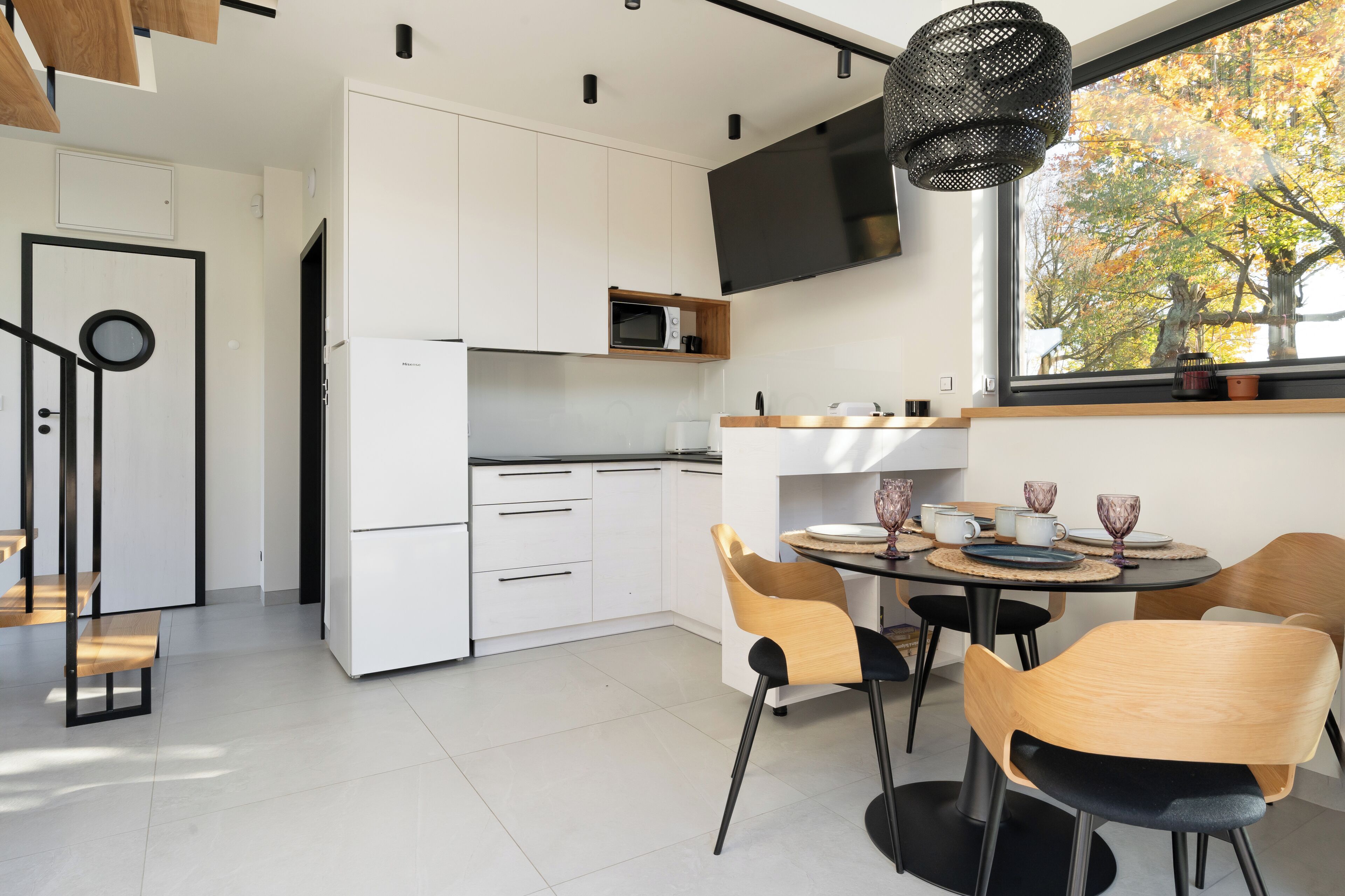 Una cucina moderna con mobili bianchi, un forno a microonde e un'ampia finestra con fogliame autunnale.