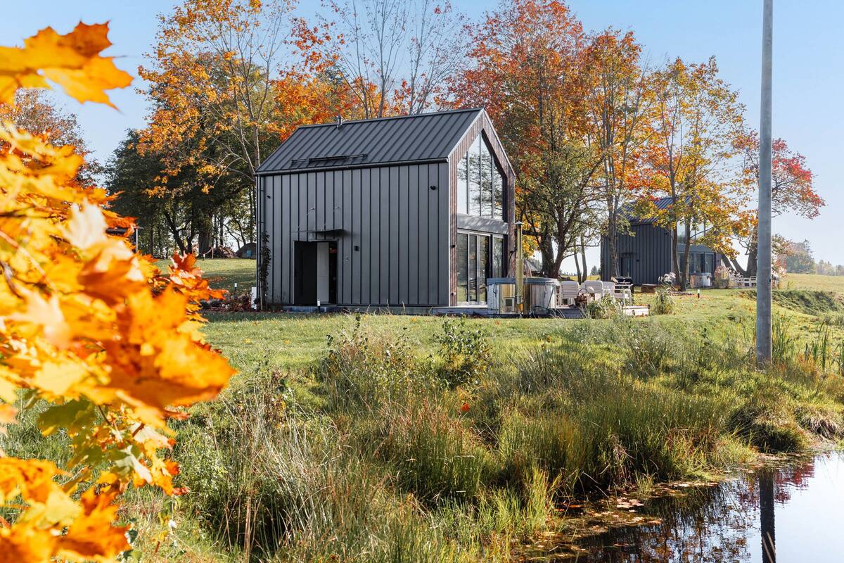 A modern house with a large garage and a small attached shed, surrounded by a grassy area and trees with autumn leaves.
