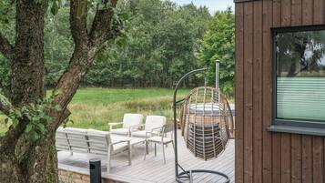 Une terrasse en bois avec des meubles d’extérieur, un fauteuil suspendu et une vue sur une zone boisée.