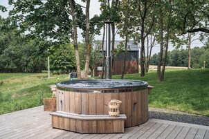 Un jacuzzi en una terraza de madera rodeado de árboles y un campo cubierto de hierba.