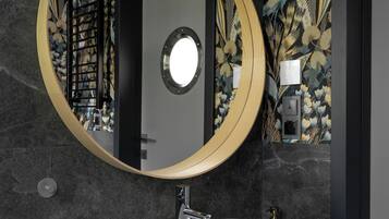 A modern bathroom with a round mirror, white sink, and dark patterned wallpaper.