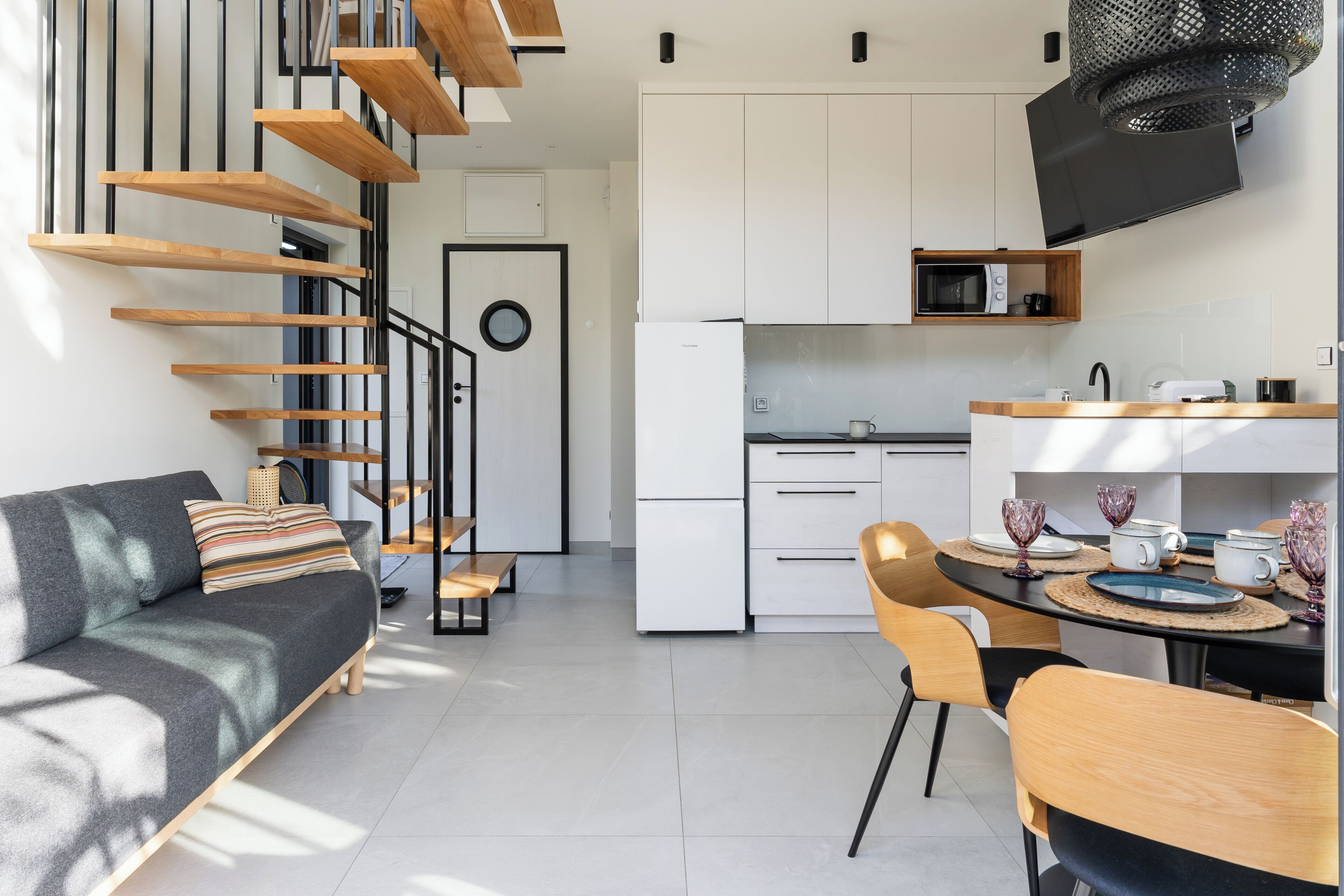 Een moderne keuken met witte kastjes, een magnetron en een eethoek met een tafel gedekt voor twee personen.
