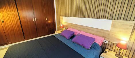 A bedroom with a large bed, wooden wardrobe, and a nightstand with a lamp.