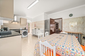 Une cuisine moderne équipée d’un four à micro-ondes, d’une cuisinière et d’un lave-linge, un coin repas avec une nappe à motifs, et une chambre à coucher avec un lit et une table de chevet.