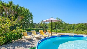 A swimming pool with a blue border, surrounded by a gravel area with yellow and white lounge chairs, and a green lawn.