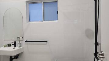 A modern bathroom with a white sink, a mirror, a shower with a handheld showerhead, and a bench.