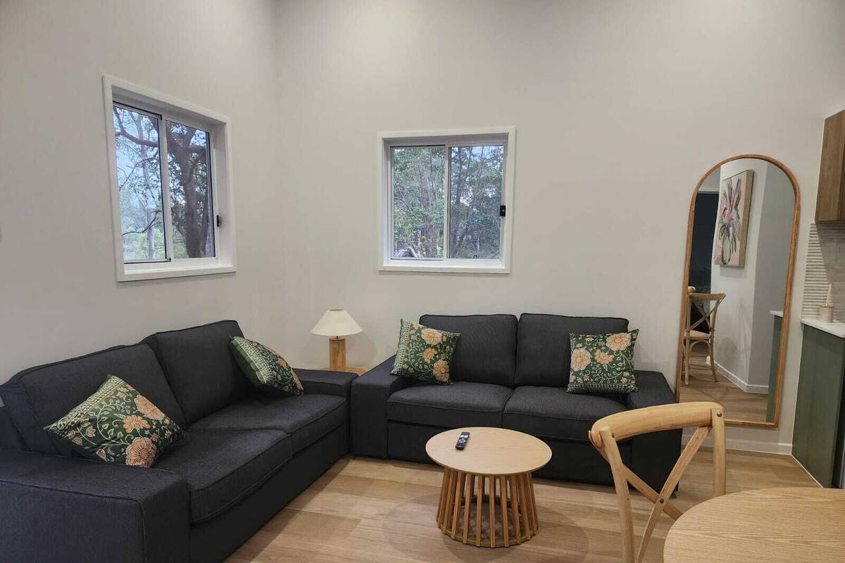A modern living room with a sectional sofa, a round wooden coffee table, and a dining area with a wooden chair.
