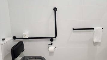 A modern bathroom with a toilet, grab bars, a towel rack, and a toilet paper holder.