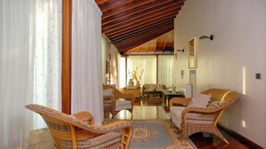 A spacious living room with a high wooden ceiling, wicker furniture, and a large window with sheer curtains. - Villa with private Pool (Ispica)