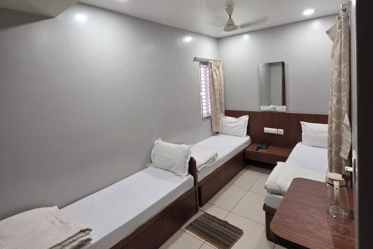 A hotel room with two single beds, a wooden desk, a mirror, and a ceiling fan.