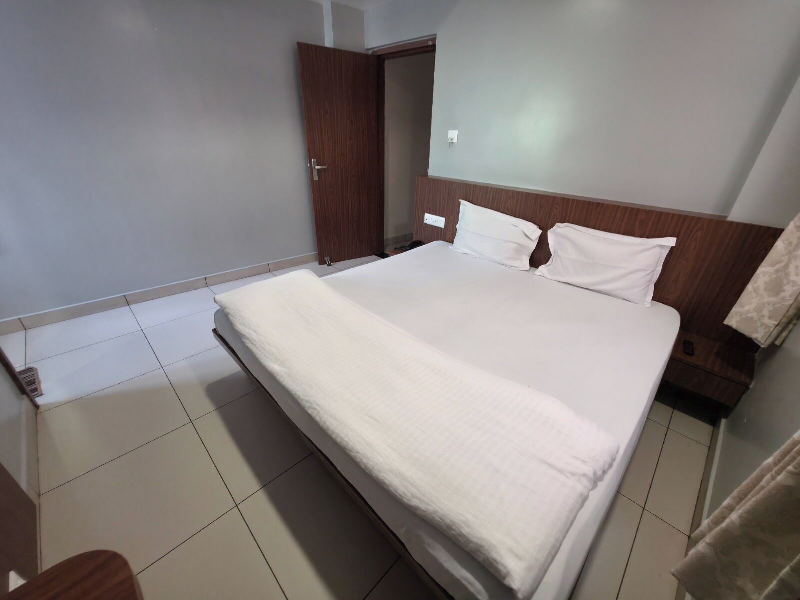 Een hotelkamer met een groot bed, een houten hoofdbord en een betegelde vloer.