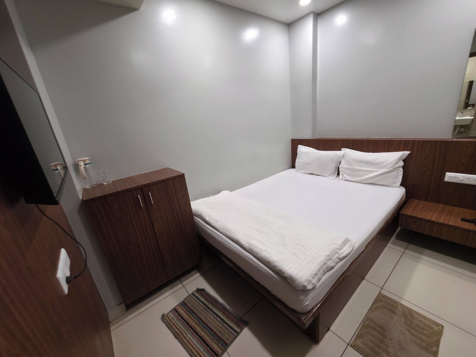 Una habitación de hotel moderna con una cama grande, un armario de madera y una mesita de noche pequeña.