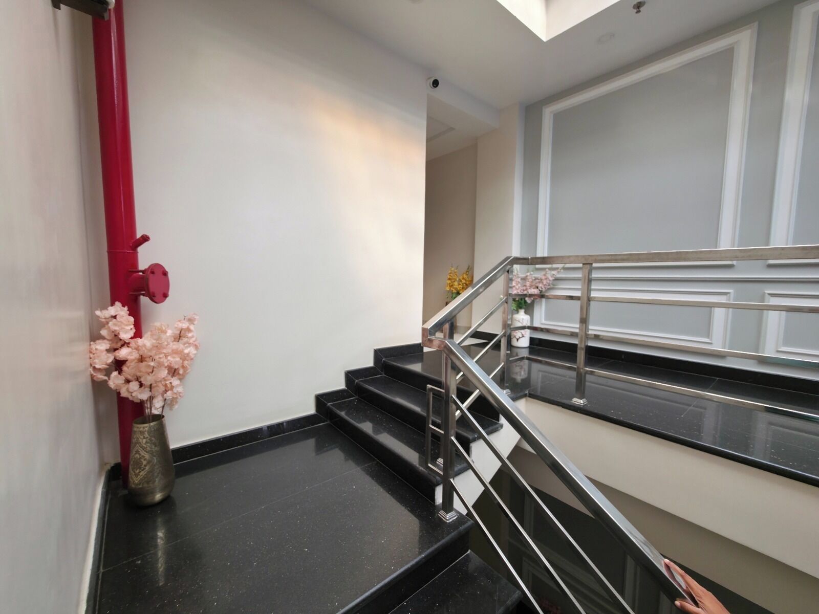 A modern staircase with a metal railing, a red pipe, and a vase with pink flowers on the landing.