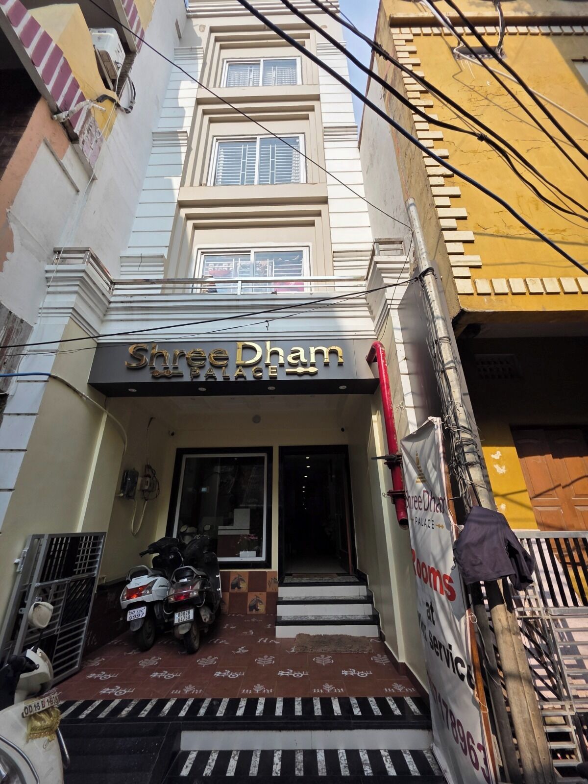 L'ingresso del Shree Dham Palace con una targa, una scala e uno scooter parcheggiato.