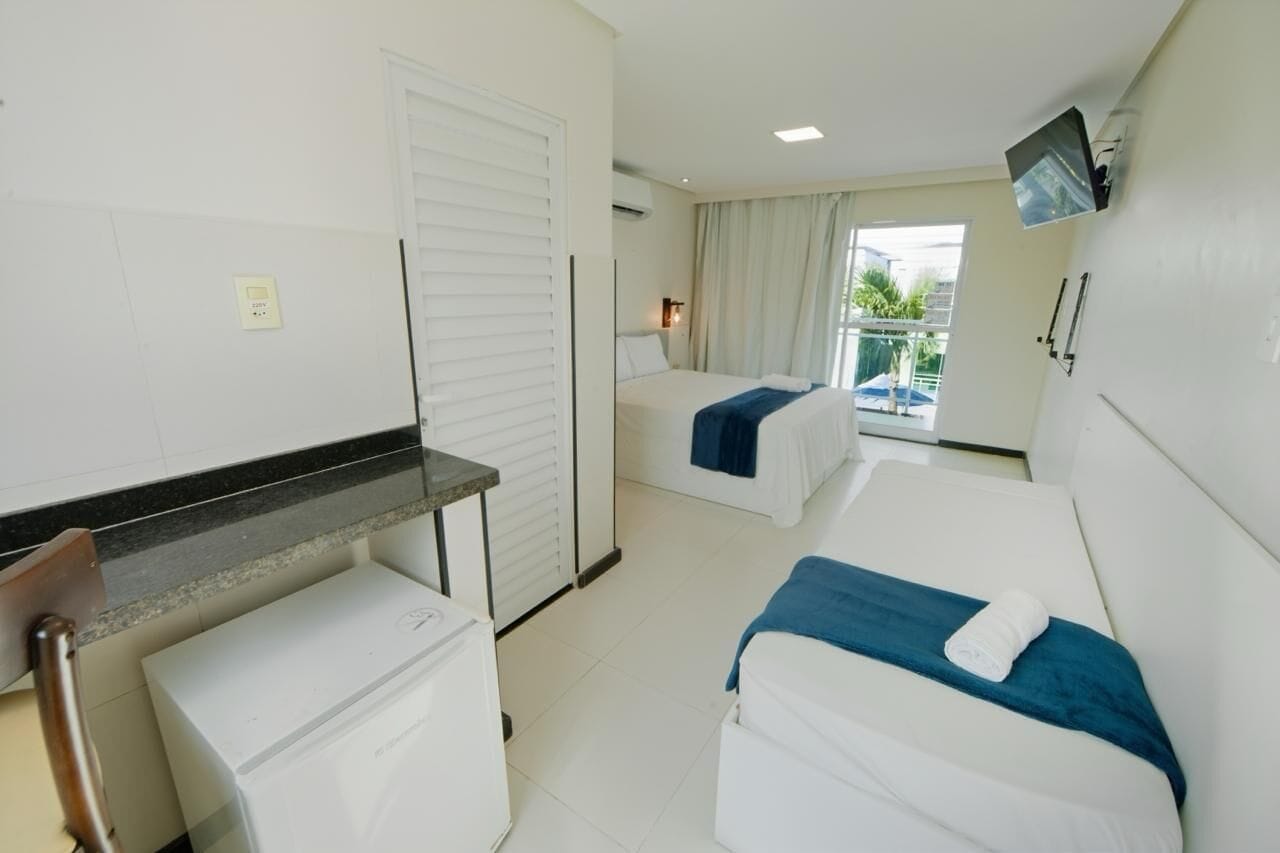 A hotel room with two beds, a small desk, a refrigerator, and a TV mounted on the wall.